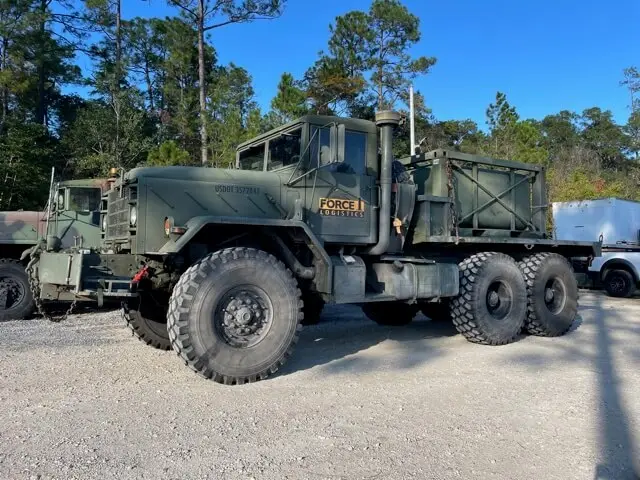Six-wheel high water truck parked under pine trees