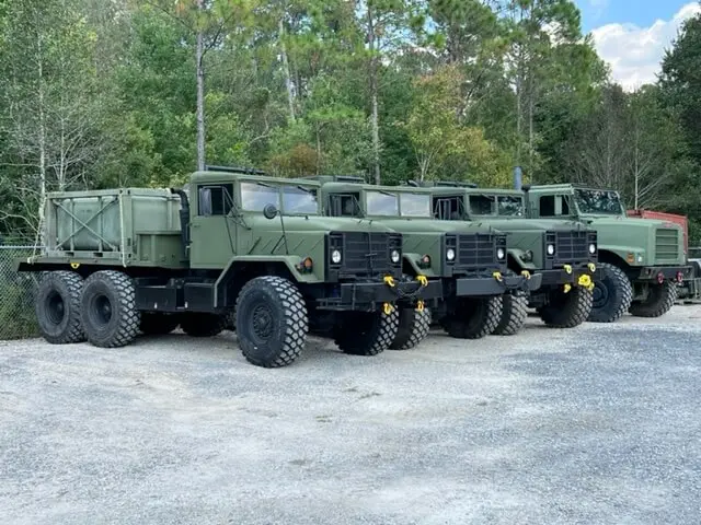 Row of green six-wheel trucks at the yard