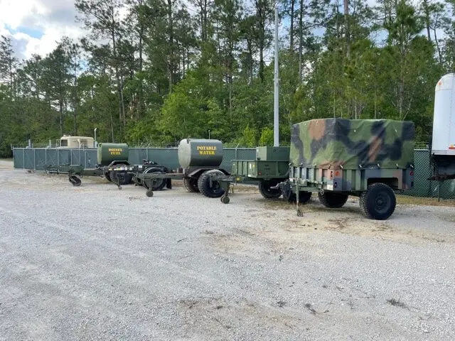 Water tank and camouflage trailers lined up at the yard