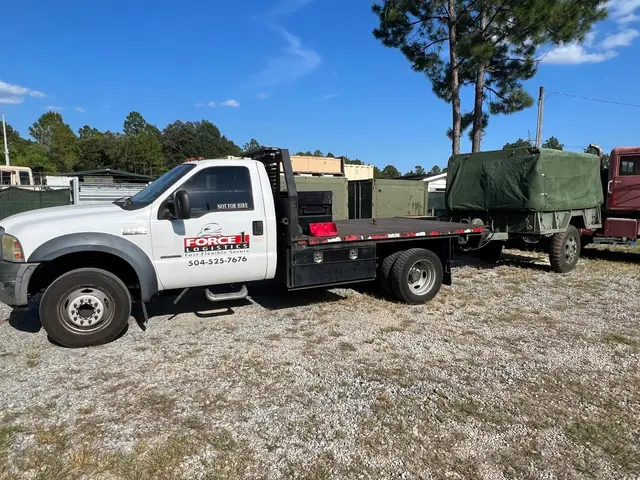 White Force 1 flatbed truck parked beside green trailers at the yard