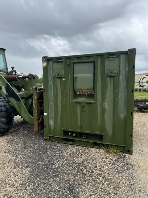 Olive green field container unit beside a loader at the yard