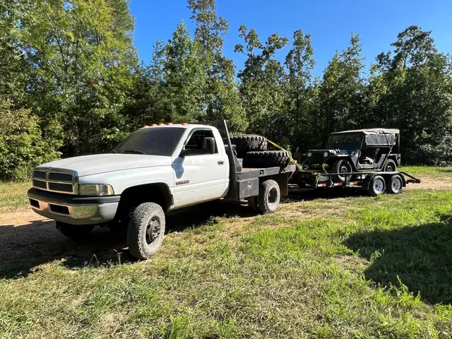 White pickup towing a trailer loaded with a military Jeep